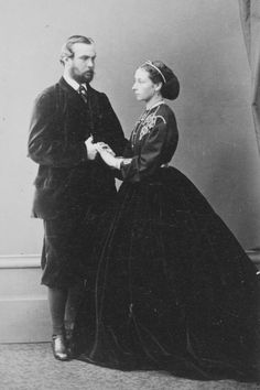 an old black and white photo of a man and woman in formal dress standing next to each other