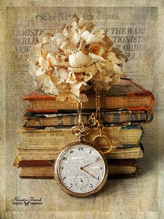 an old pocket watch sitting on top of some books with flowers in the middle and a chain attached to it