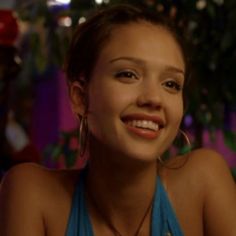 a young woman wearing large hoop earrings and smiling at the camera while sitting in front of a potted plant