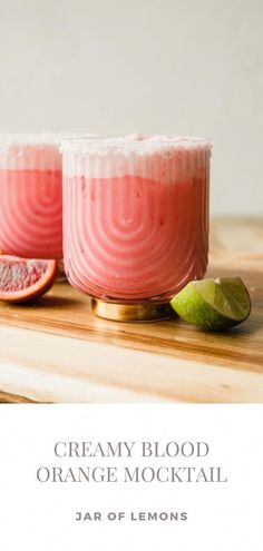 two glasses filled with orange and blood orange mojita on top of a wooden table