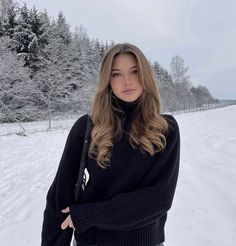 a woman standing in the snow with her arms crossed and looking off to the side