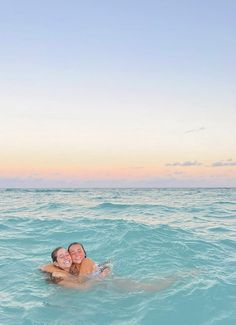 two people are swimming in the ocean at sunset or dawn with their arms around each other