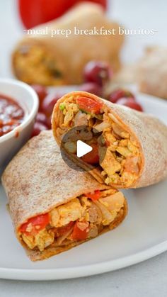 a burrito cut in half on a plate next to a bowl of salsa and tomatoes