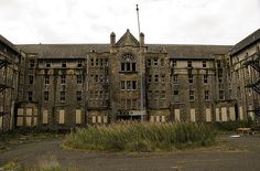 an old building with lots of windows and grass in the foreground, on a cloudy day