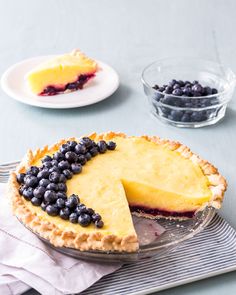 a blueberry cheesecake on a plate next to a bowl of blueberries and another pie