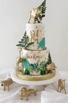 a three tiered cake decorated with gold and green leaves, giraffes and palm leaves