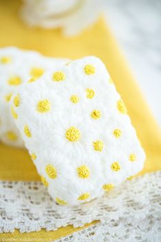 two crocheted yellow and white squares sitting on top of a doily covered table