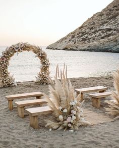 a wooden bench sitting on top of a sandy beach next to an arch covered in flowers