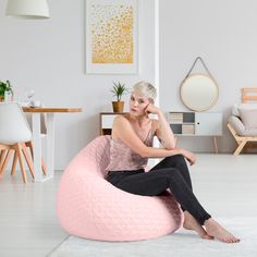 a woman sitting on a pink bean bag chair in a living room with white walls