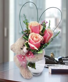 a teddy bear sitting on top of a table next to a vase filled with flowers