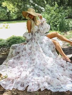 a woman in a white dress and hat sitting on a tree stump with her legs crossed