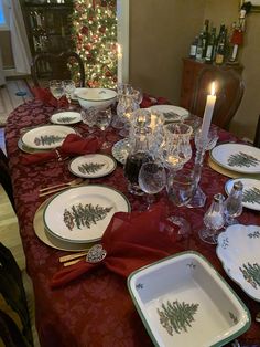 a dining room table set for christmas with plates and glasses on it, lit by a candle