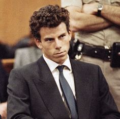 a man in a suit and tie sitting at a table with his hands folded out