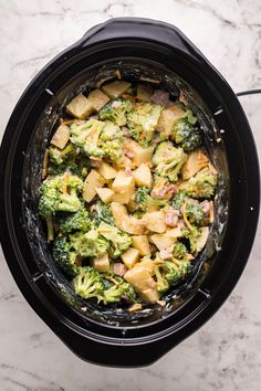 a crock pot filled with broccoli, potatoes and ham in it on a marble counter top