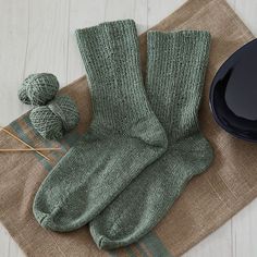 a pair of green socks sitting on top of a table next to knitting needles and balls of yarn