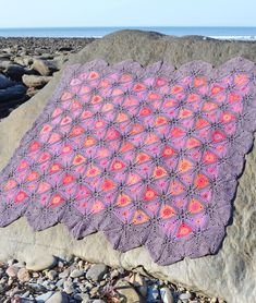 a purple crocheted blanket sitting on top of a rock next to the ocean