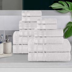 a stack of white towels sitting on top of a counter next to a green plant