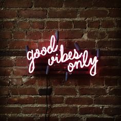 a neon sign that says good vibes only on a brick wall