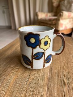 a coffee cup with blue and yellow flowers on it sitting on a table next to a chair