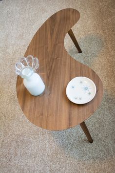 a wooden table with a glass vase and plate on the top, sitting on carpeted floor