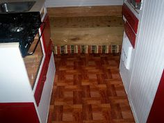 small kitchen with red and white cabinets and wood flooring on the walls, along with a stove top oven