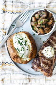 steak, baked potatoes and mushrooms are on a plate with a fork next to it