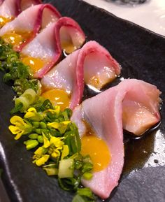 some food is laying out on a black plate with yellow flowers in the middle and green leaves around it