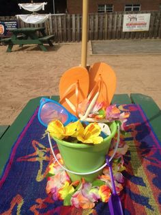 a green bucket filled with flowers on top of a blue table cloth next to an umbrella