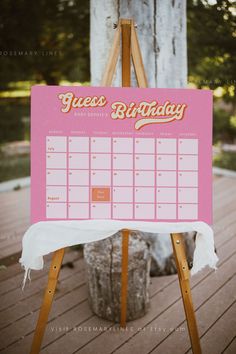 a wooden easel holding a pink and white birthday calendar on it's side