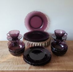 a table topped with purple glass dishes and cups on top of a wooden table next to a white wall