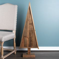 a wooden christmas tree sitting next to a white chair in a room with blue walls