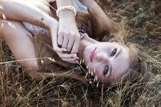 a woman laying in the grass with her hands on her face and arm around her body