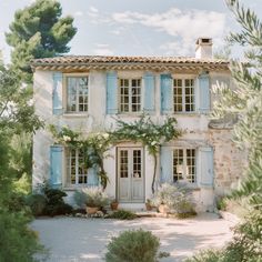 an old stone house with blue shutters on the front door and windows, surrounded by greenery