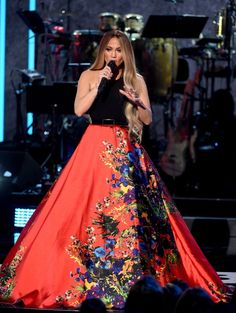 the singer is dressed in an orange and blue floral dress while holding a microphone to her mouth