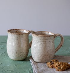 two coffee mugs sitting on top of a table next to a cookie biscuit