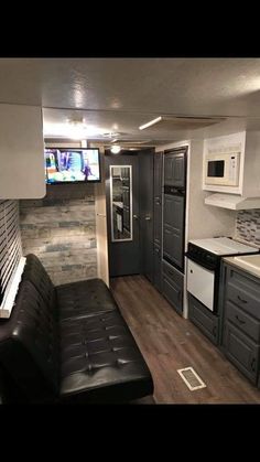 a living room and kitchen area in a mobile home with wood flooring, black leather couch