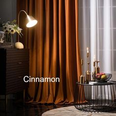 a table with some fruit on it in front of a curtained window and a lamp