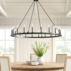 a chandelier hanging over a dining room table with chairs and vases on it