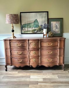 an old dresser is painted pink with gold hardware and has a painting on the wall above it