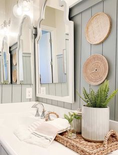 a white sink sitting under a bathroom mirror next to a potted plant on top of a counter