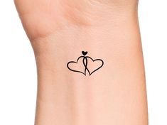 a small tattoo on the wrist of a woman with two hearts and an arrow in the center