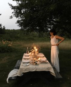 a woman standing next to a table with food on it in the middle of a field