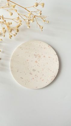 a white plate sitting on top of a table next to a flower vase and dried plant