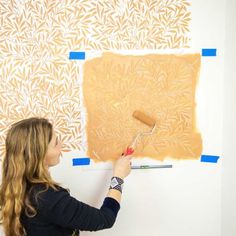 a woman is painting a wall with orange and white designs on it, while holding a paint roller in her hand