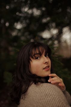 a woman is posing for a photo in front of some trees with her hand on her chin