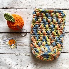 a crocheted pouch sitting next to an orange on a white wooden table with a keychain