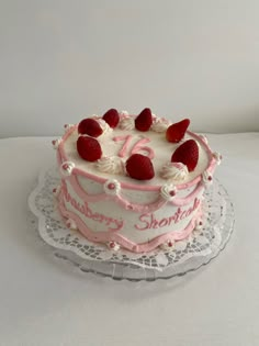 a birthday cake with strawberries on top is sitting on a lace doily and sits on a white tablecloth