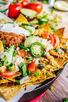 nachos with meat, cheese and vegetables in a skillet on a table