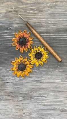 three sunflowers are sitting on a wooden table with a sewing needle in the middle