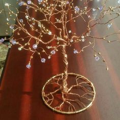 a wire tree with blue and white beads on it sitting on a wooden table in front of a window